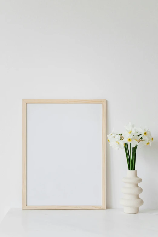 a picture frame sitting on top of a table next to a vase of flowers, postminimalism, cream white background, promo image, whiteboards, vanilla - colored lighting