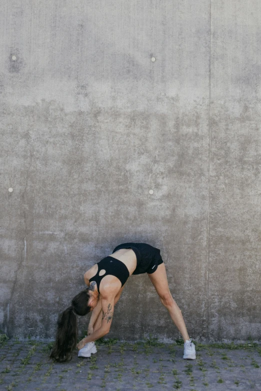 a woman doing a handstand in front of a wall, by Jessie Algie, sport bra and shorts, unsplash photography, cement, folded