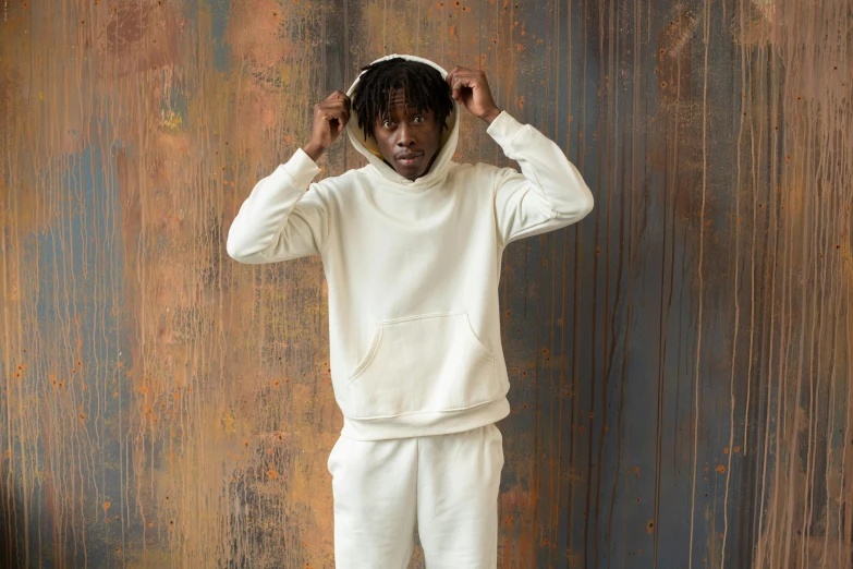 a man standing in front of a rusty wall, an album cover, inspired by Thomas Blackshear, wearing a hoodie and sweatpants, pearlescent white, kara walker james jean, thumbnail