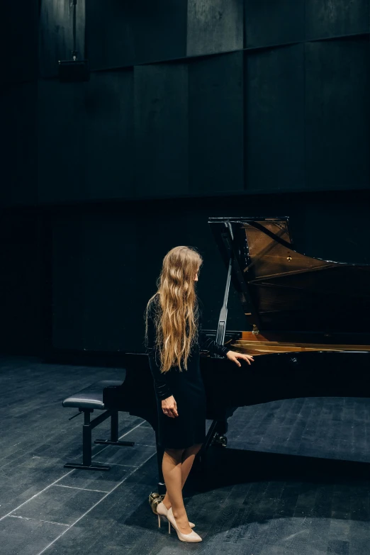 a woman standing next to a piano on a stage, unsplash contest winner, with long blond hair, university, right hand side profile, facing away