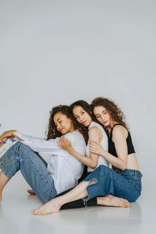 three women sitting next to each other on the floor, trending on pexels, antipodeans, arm around her neck, in front of white back drop, ( ( ( wearing jeans ) ) ), bisexual lighting