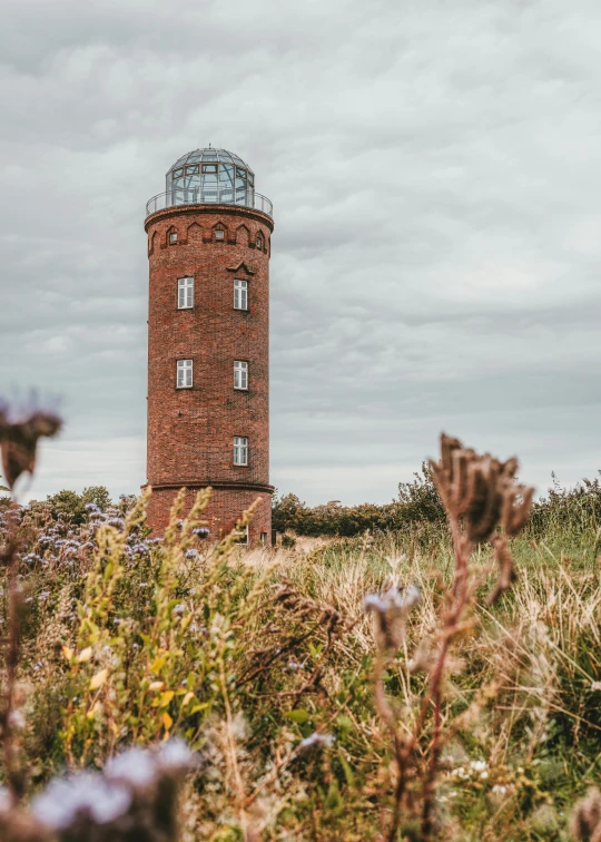 a tall tower sitting on top of a lush green field, by Matthias Stom, unsplash contest winner, light house, brick, brown, panoramic