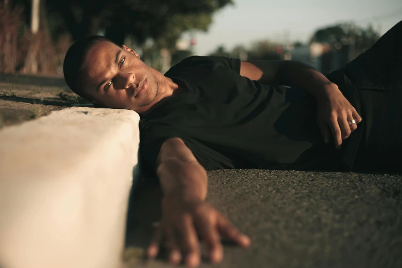 a man laying on the ground next to a cement wall, pexels contest winner, happening, film still of barack obama, man is with black skin, standing in road, depressed dramatic bicep pose