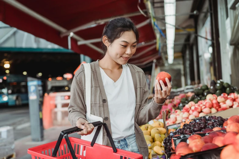 a woman looking at her cell phone while standing in front of a fruit stand, pexels contest winner, 2 5 6 x 2 5 6 pixels, australian, getting groceries, a young asian woman