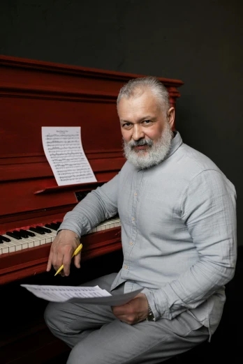 a man sitting in front of a red piano, gray beard, sofya emelenko, official photo, photo”