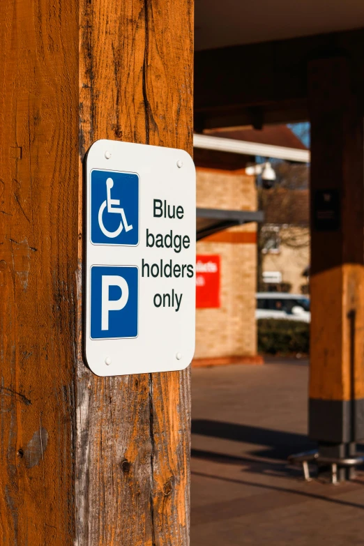 a blue and white sign on a wooden pole, by Paul Bird, unsplash, wheelchair, cars parked, square, brown