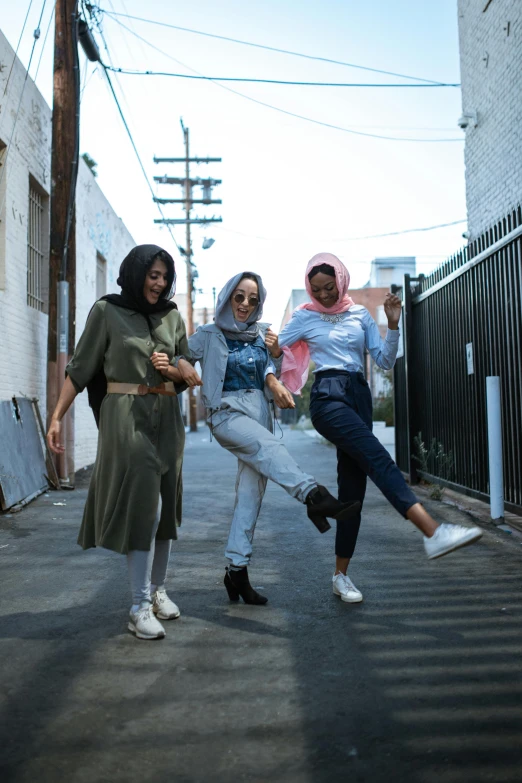 a group of women standing next to each other on a street, trending on unsplash, hijab, jump pose, los angeles ca, three women