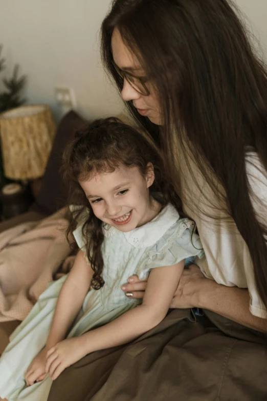 a woman sitting on top of a bed next to a little girl, girl with dark brown hair, turning her head and smiling, textured, trending ，