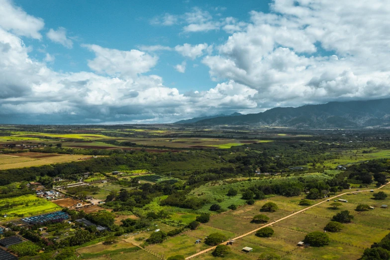 an aerial view of a lush green valley, pexels contest winner, maui, green field with village ruins, panoramic widescreen view, clouds and fields in background