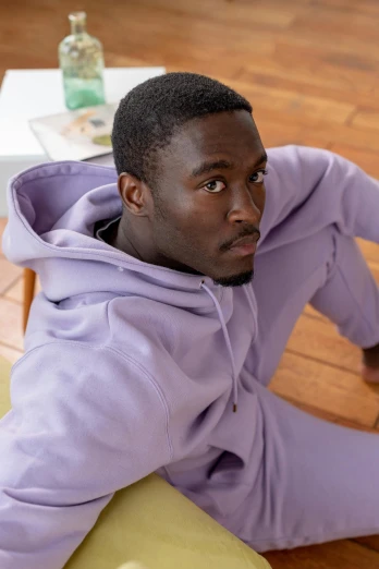 a man sitting on a couch with a remote in his hand, an album cover, inspired by Paul Georges, trending on pexels, happening, wearing a purple sweatsuit, model posing, mkbhd, pastels