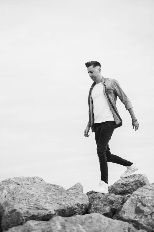 a black and white photo of a man walking on rocks, by Chase Stone, realism, singer maluma, clean background, julian ope, mac miller