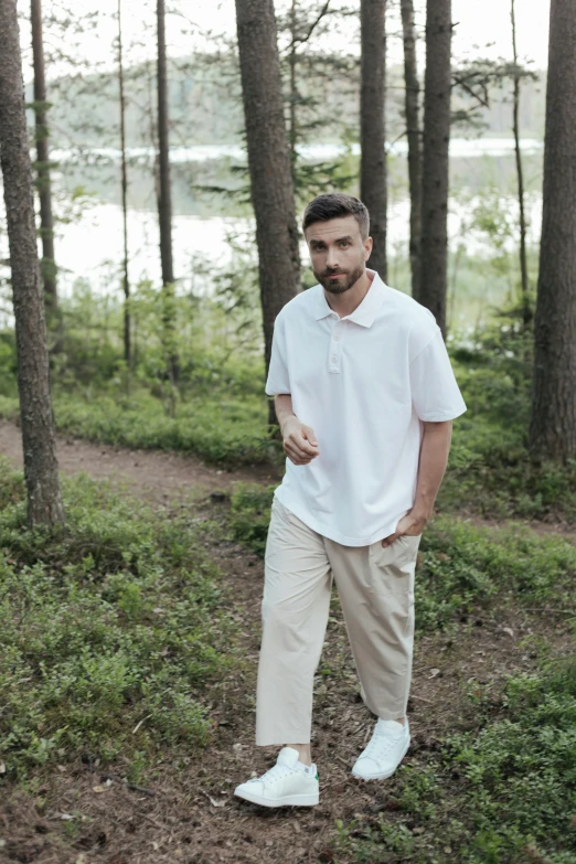 a man standing in the middle of a forest, wearing polo shirt, trendy white clothing, nikolay, feature