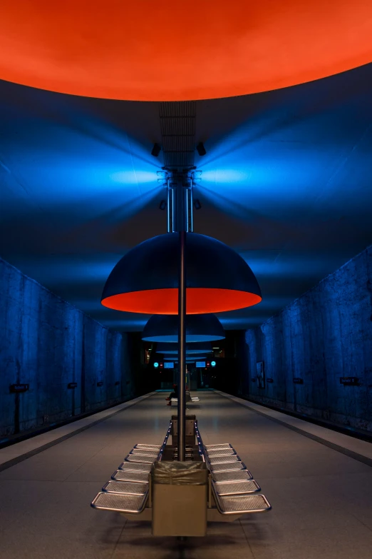 a red umbrella sitting in the middle of a tunnel, by Jens Søndergaard, blue lamps on the ceiling, zenithal lighting, station, blue and orange lighting