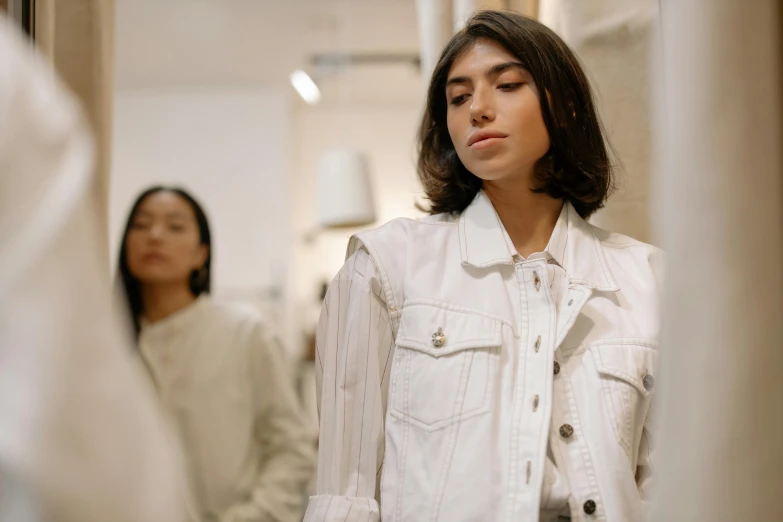 a woman standing in front of a mirror, trending on pexels, realism, white jacket, fashion show photo, uniform off - white sky, thumbnail