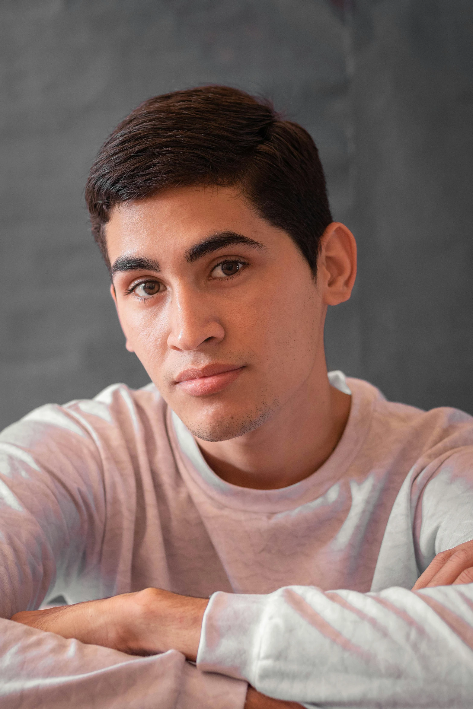 a young man sitting at a table with his arms crossed, inspired by John Luke, pexels contest winner, hispanic, androgynous face, catalog photo, headshot profile picture