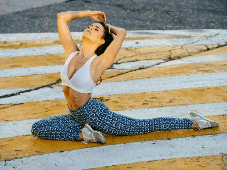 a woman stretching in the middle of a crosswalk, arabesque, leggings, patterned, sits on a rooftop, physical : tinyest midriff ever