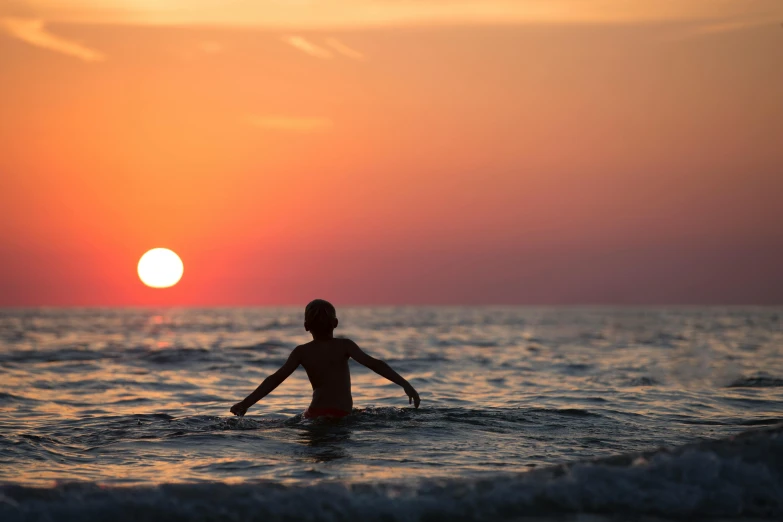 a woman standing in the ocean at sunset, a picture, unsplash contest winner, renaissance, surfing, little kid, orange sun set, cardboard