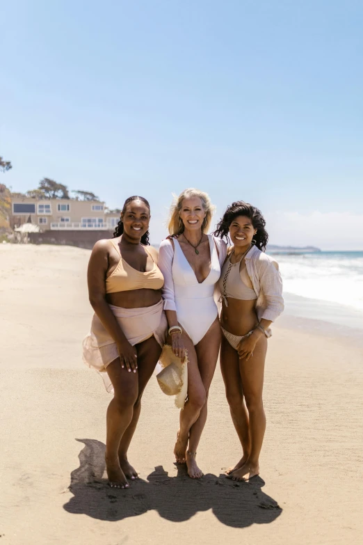 three women standing next to each other on a beach, golden skin tone, southern california, goop, skintight suits