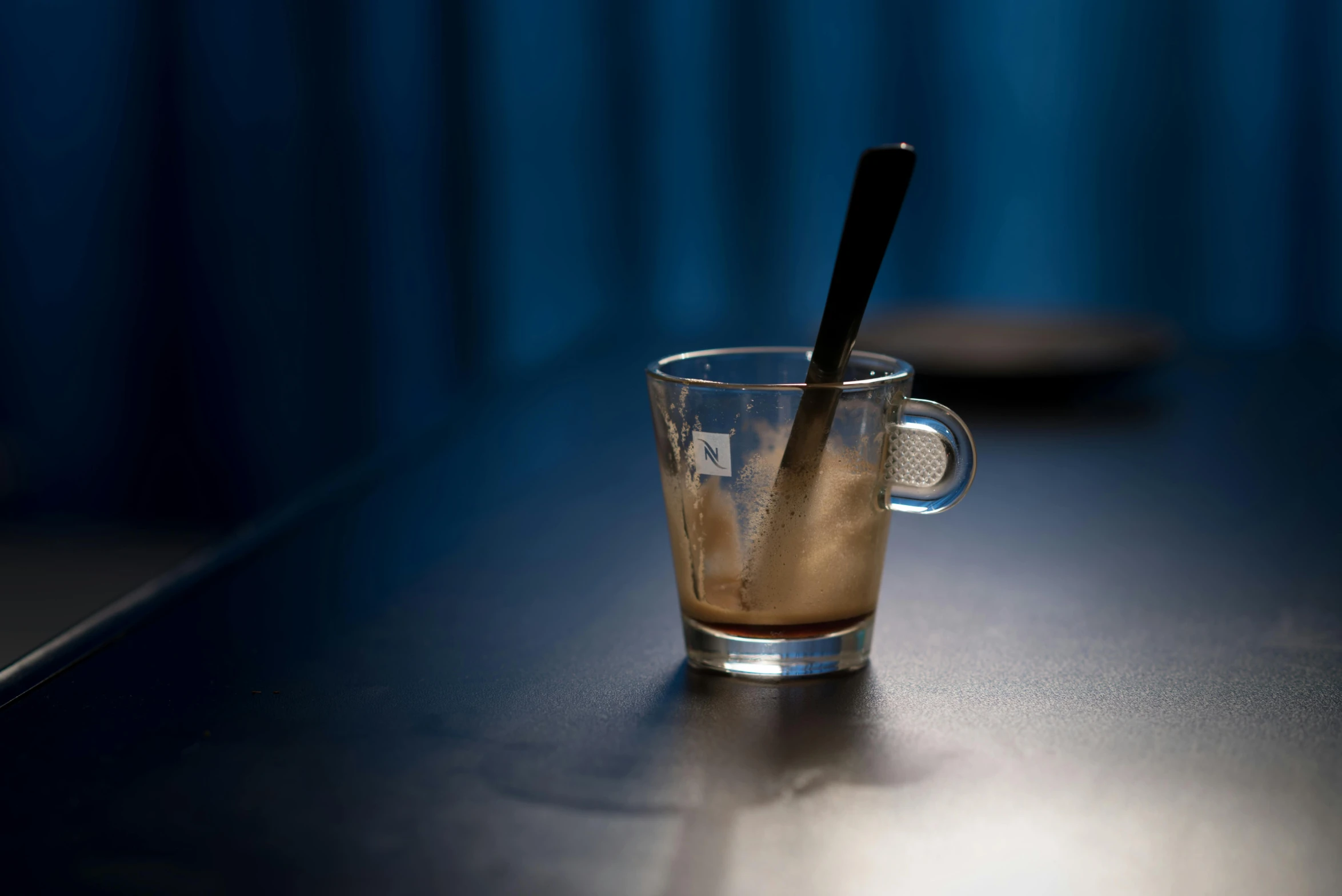 a close up of a cup of coffee on a table, with blue light inside, spoon, sitting alone at a bar, cold brew coffee )