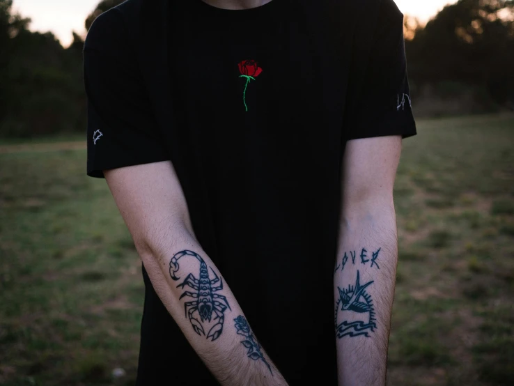 a man standing in a field with tattoos on his arms, pexels contest winner, black rose, black t shirt, loish |, plain background