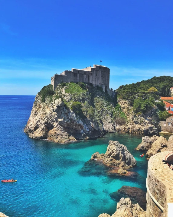 a castle sitting on top of a cliff next to the ocean, boats in the water, square, jeszika le vye, slide show