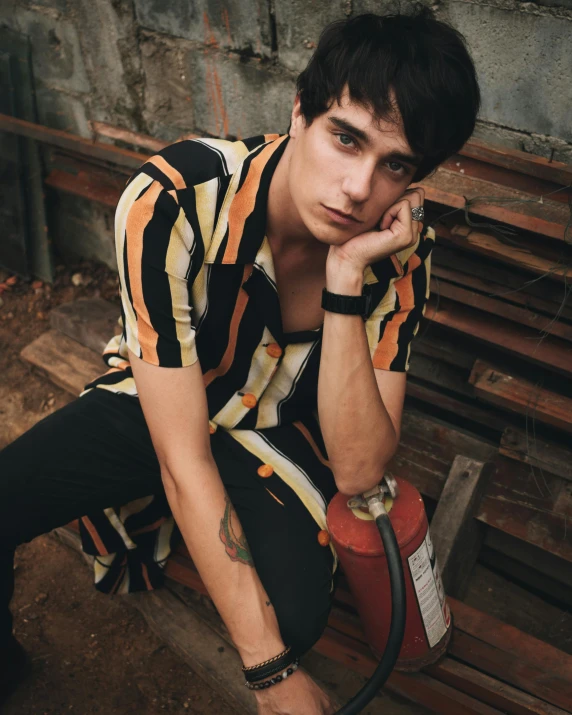 a man sitting on a bench next to a fire hydrant, an album cover, inspired by John Luke, trending on pexels, nonbinary model, looking serious, david marquez, patterned clothing