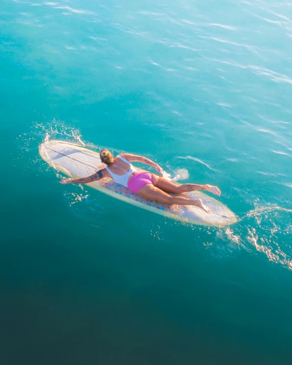 a woman riding a surfboard on top of a body of water, from above