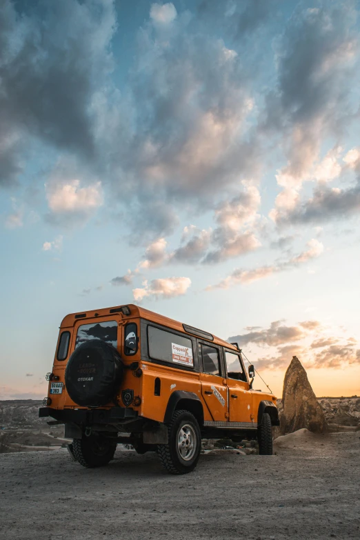 an orange jeep parked on top of a dirt field, pexels contest winner, renaissance, land rover defender 110 (1985), tall big rocks, late afternoon lighting, square