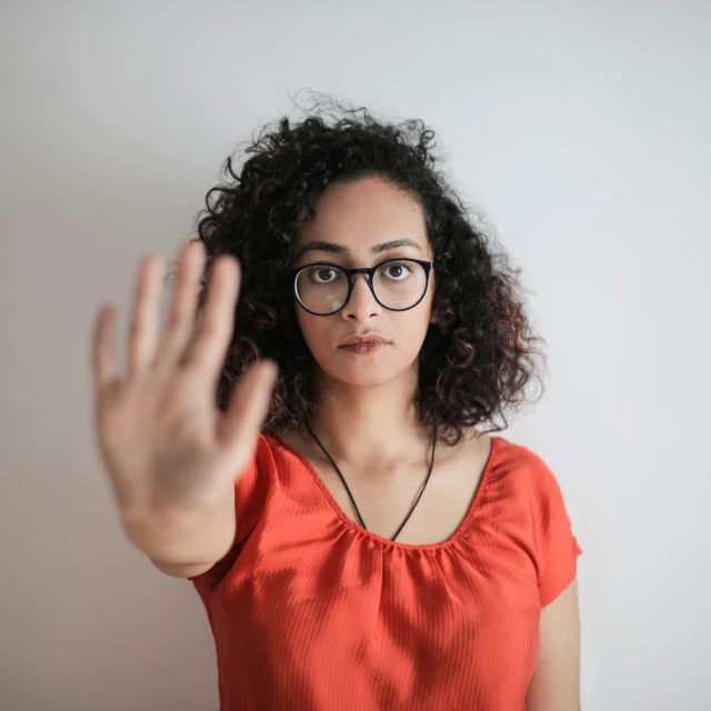 a woman wearing glasses making a stop sign, pexels, antipodeans, aida muluneh, women hand, 7 0 mm portrait, curly haired