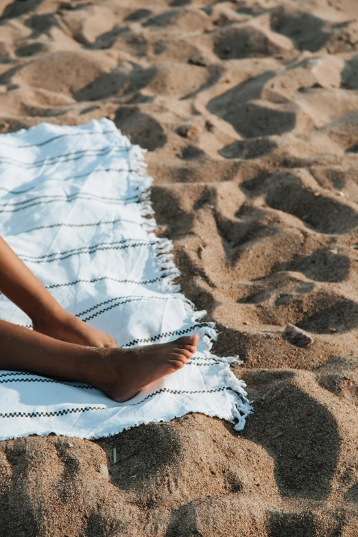 a woman sitting on a towel on the beach, zoomed in, sustainable materials, less detailing, middle shot