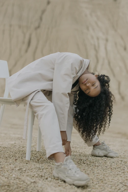 a woman sitting on top of a white chair, inspired by Afewerk Tekle, trending on unsplash, renaissance, wearing a track suit, covered in sand, her hair flowing down, on ground