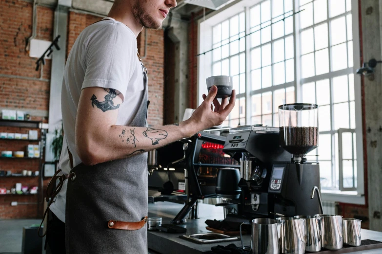 a man standing in front of a coffee machine, by Everett Warner, pexels contest winner, tattooed, white waist apron and undershirt, avatar image, profile image