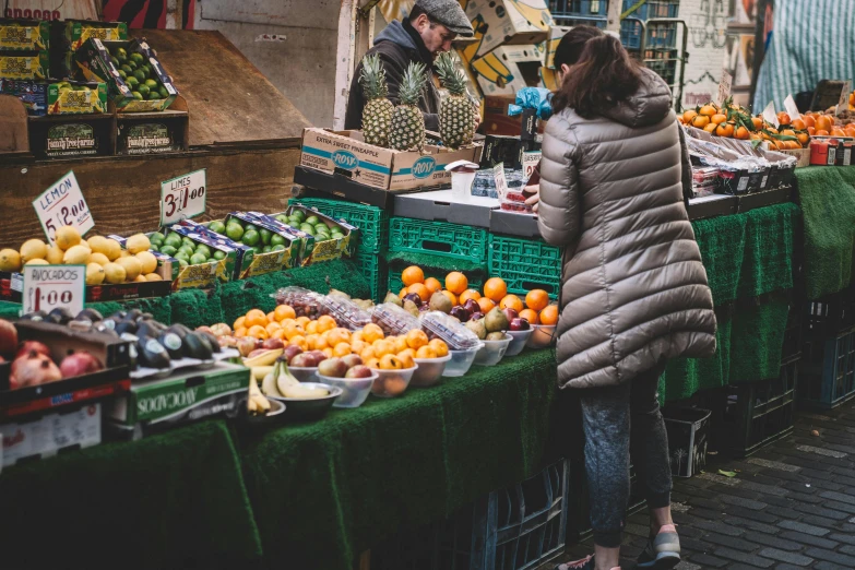 a woman standing in front of a fruit stand, pexels contest winner, facing away, 🦩🪐🐞👩🏻🦳, people shopping, farmer's market setting