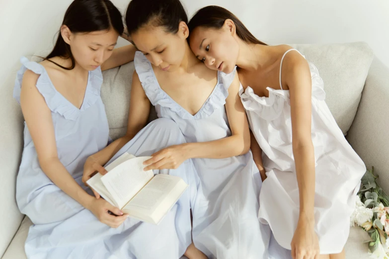 three women sitting on a couch reading a book, inspired by Fei Danxu, happening, wearing a nightgown, blue soft details, photoshoot for skincare brand, closeup - view