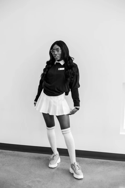 a woman standing in front of a white wall, a black and white photo, by Andrew Stevovich, unsplash, dressed as schoolgirl, sza, white miniskirt, young thug