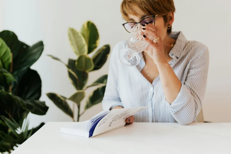 a woman sitting at a table drinking a glass of water, pexels contest winner, reading engineering book, plants in glasses, with a white background, head to waist