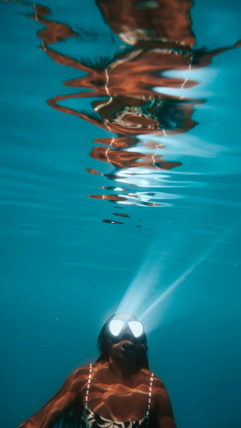 a woman swims under the surface of the water, by Daren Bader, pexels, photorealism, boat with lamp, scuba mask, high detailed light refraction, high angle close up shot