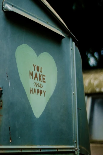 a green mailbox with a sticker that says you make me happy, a photo, graffiti, full heart - shaped face, tiny house, subtitles, color film still