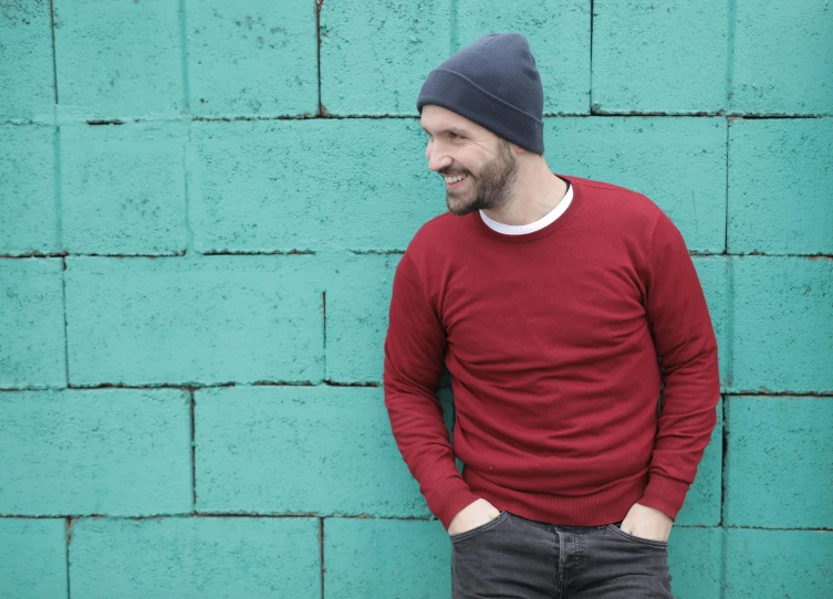 a man standing in front of a green brick wall, inspired by Juan O'Gorman, pexels contest winner, wearing teal beanie, red sweater and gray pants, charlie cox, indigo and venetian red