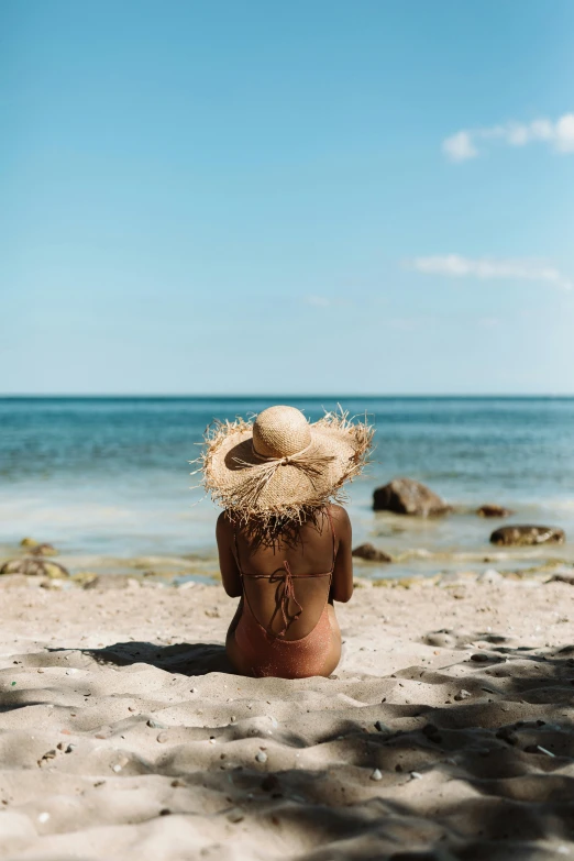 a woman sitting on top of a sandy beach, facing away from the camera, straw hat, sunbathed skin, profile image