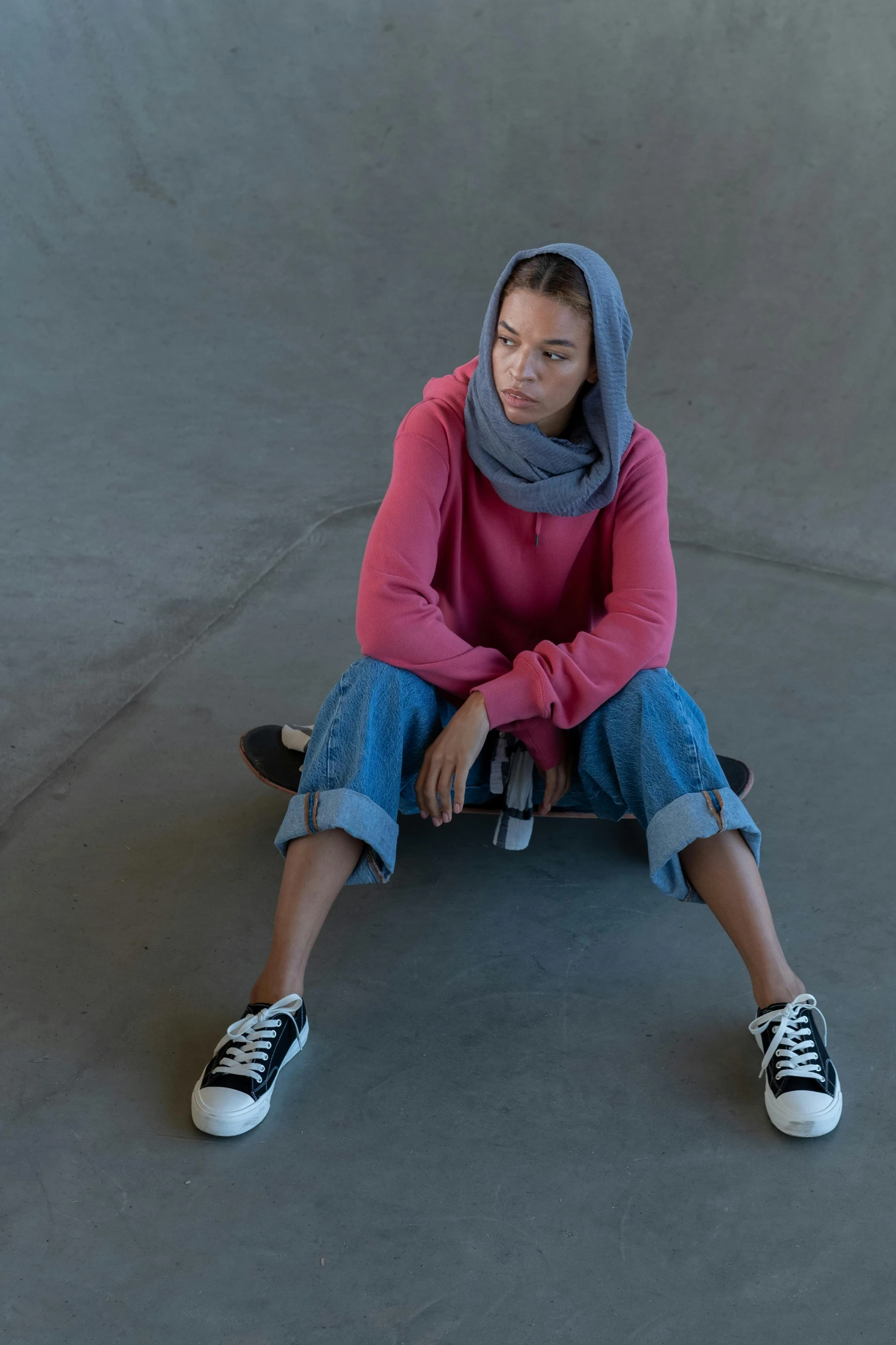 a woman sitting on a skateboard in a skate park, unsplash contest winner, renaissance, wearing a head scarf, wearing a pink hoodie, red sweater and gray pants, nonbinary model