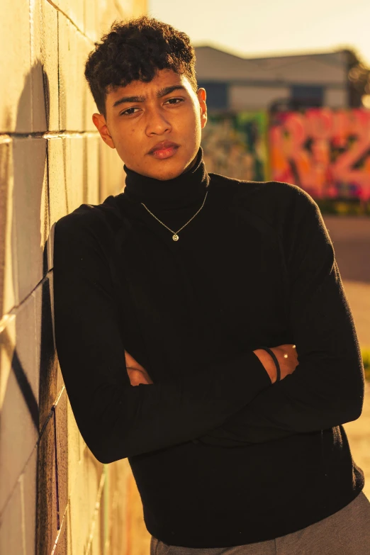 a man leaning against a wall with his arms crossed, featured on instagram, black turtle neck shirt, non binary model, (golden hour), teenager