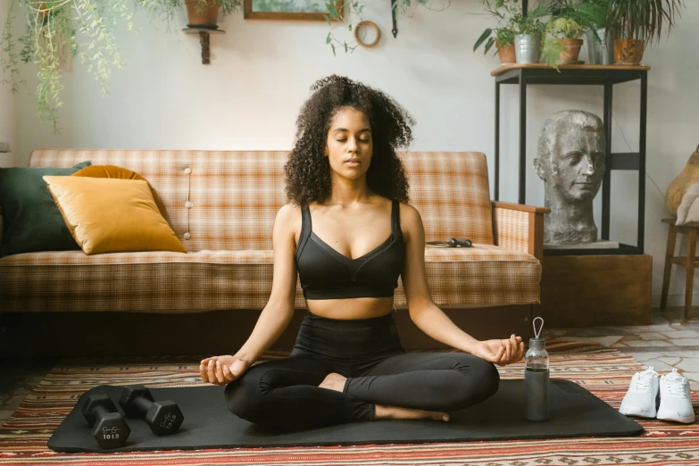 a woman sitting on a yoga mat in a living room, trending on pexels, afrocentric mysticism, paradise garden massage, wearing black tight clothing, a cyborg meditating