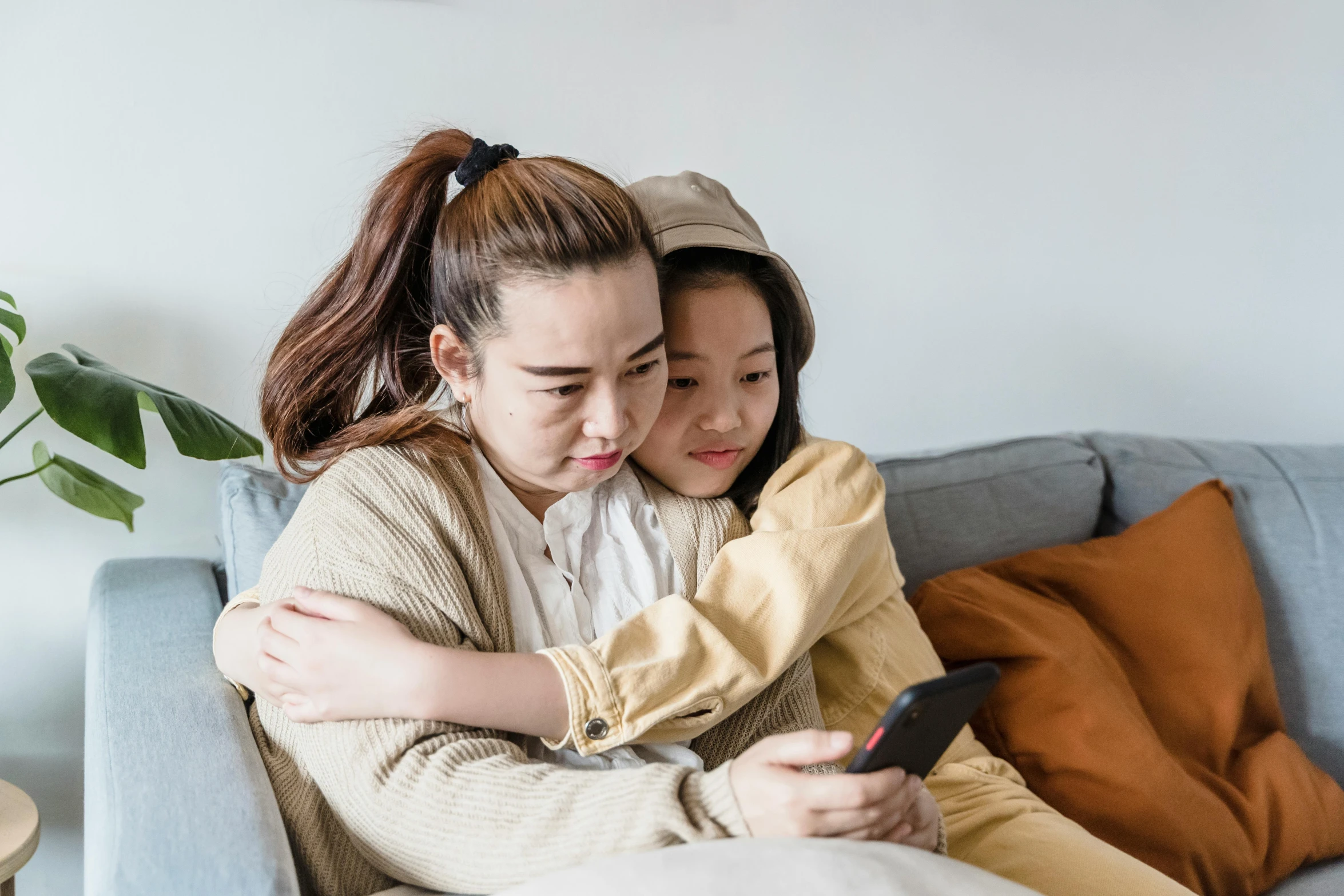 a couple of women sitting on top of a couch, a cartoon, trending on pexels, incoherents, young asian girl, mourning family, she is holding a smartphone, hugs