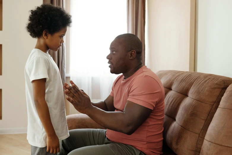 a little boy standing next to a man on a couch, pexels, hurufiyya, arguing, ( ( dark skin ) ), a broad shouldered, australian