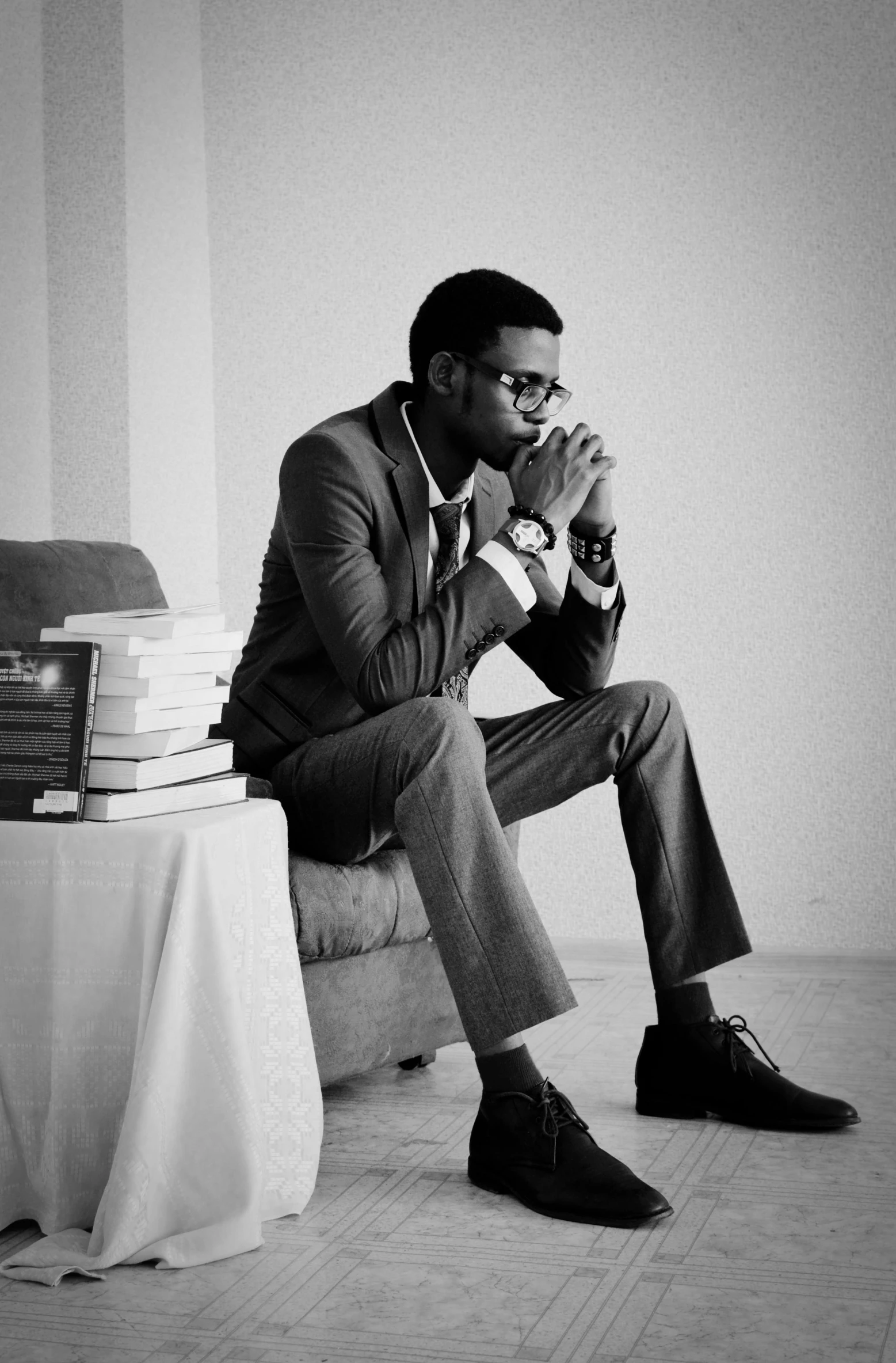 a black and white photo of a man sitting on a couch, an album cover, unsplash, romanticism, wearing a suit and glasses, black man, young man, sitting in the classroom