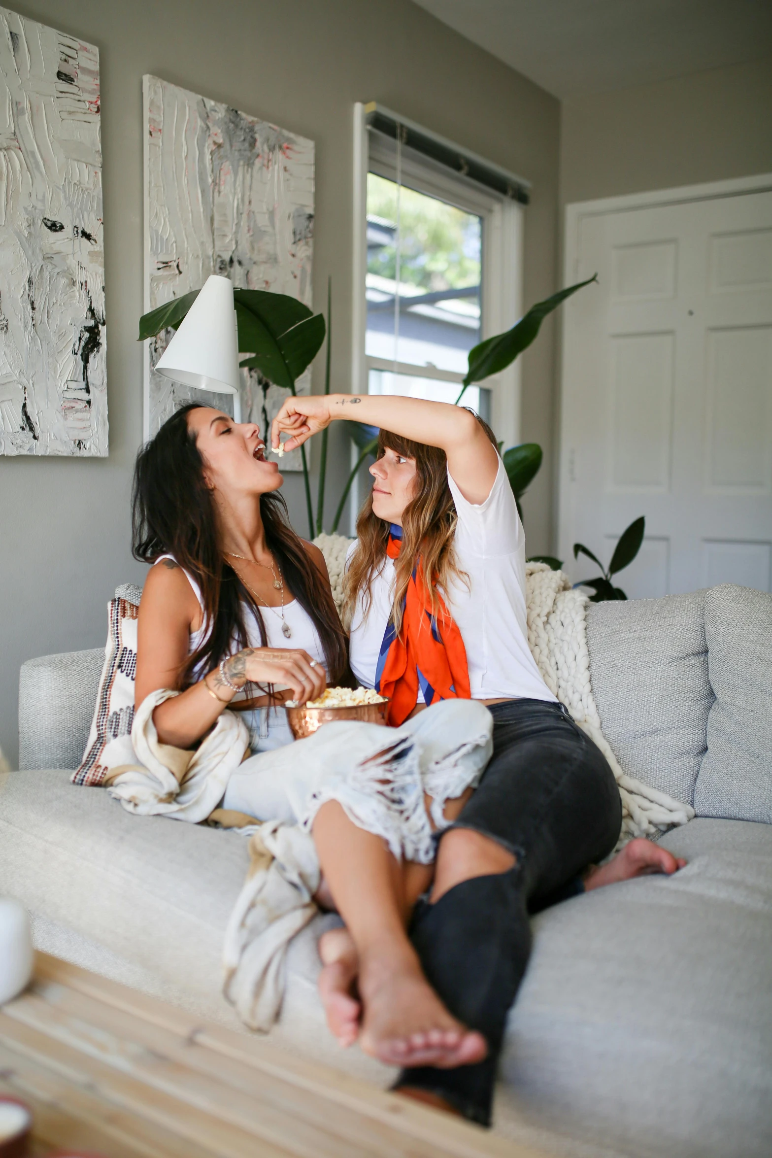 a couple of women sitting on top of a couch, a picture, by Jessie Algie, trending on unsplash, eating cheese, party hats, white l shaped couch, 🍸🍋