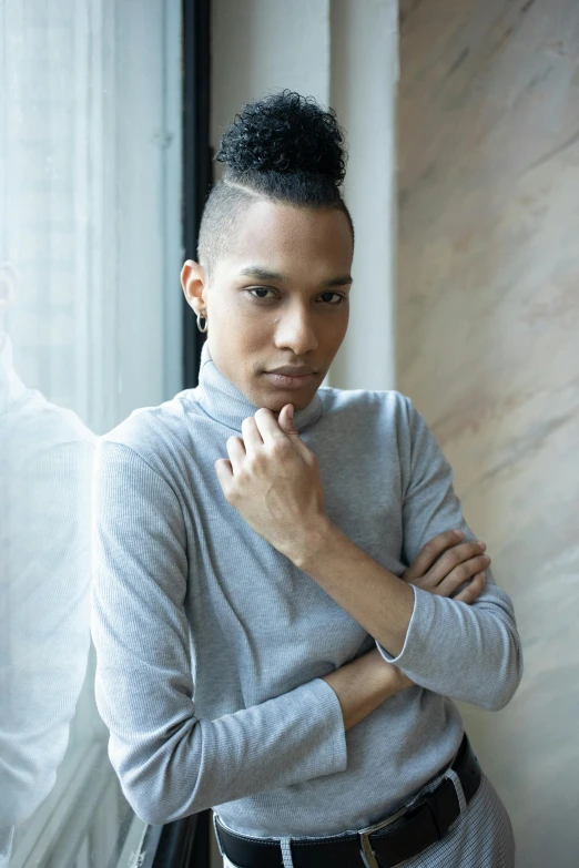 a man standing next to a window with his hand on his chin, a portrait, by William Berra, unsplash, beautiful androgynous girl, african american, iris van herpen rankin, he is wearing a brown sweater