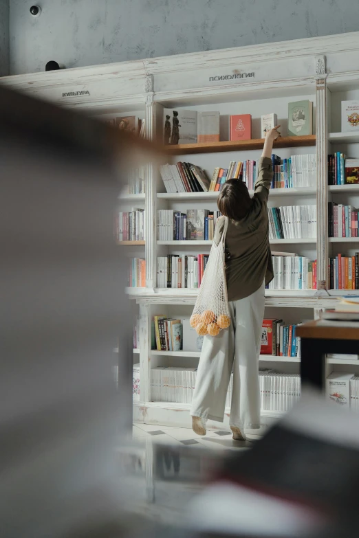 a woman standing in front of a bookshelf holding a bag, happening, upshot, shot from a distance, full width, raising an arm