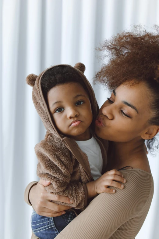 a woman holding a baby in her arms, by Lily Delissa Joseph, pexels, renaissance, mixed-race woman, black haired girl wearing hoodie, caramel, with textured hair and skin